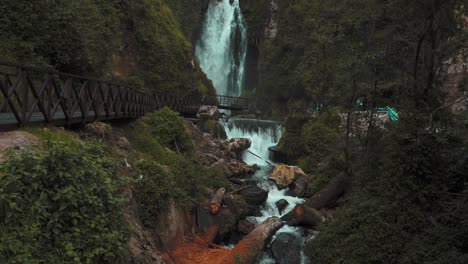 Langsame-Neigung-Nach-Oben-Blick-Auf-Den-Kaskadierenden-Peguche-wasserfall-Mit-Holzstegbrücke-In-Otavalo,-Ecuador