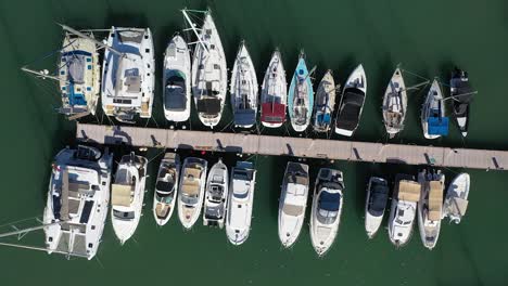 Harbor-with-moored-sailing-boats-to-the-pier-at-Latchi-port,-aerial-rise-up-view