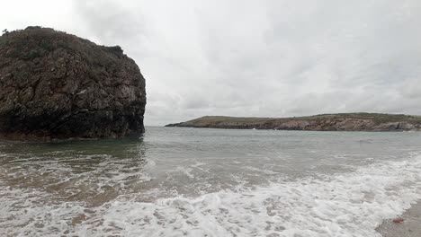 Meereswellen-In-Zeitlupe,-Die-Um-Eine-Große-Felseninsel-An-Der-Küste-Von-Anglesey-Spritzen