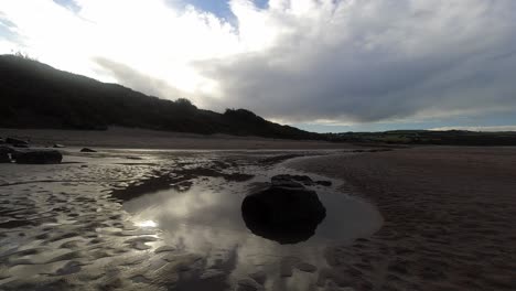 Time-lapse-shimmering-sunset-beach-rock-pool-clouds-passing-above-woodland-coastline