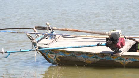 Weathered-Boat-With-Engine-Propeller-Resting-Out-Of-Water-On-River