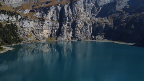Filmische-Luftaufnahme-über-Den-Oeschinensee-Und-Den-Wunderschönen-Wald-Und-Die-Berge,-Die-Ihn-Umgeben,-An-Einem-Sonnigen-Tag-Und-Das-Türkisfarbene-Wasser-Zu-Schätzen