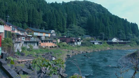 Peaceful-scene-of-remote-Japanese-village-on-riverside-surrounded-by-forest---static-view-in-Kirishima,-Japan