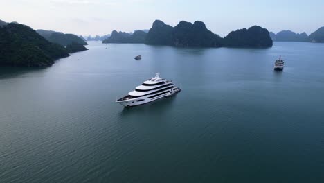 aerial-of-beautiful-white-luxury-yacht-anchored-in-Ha-Long-Bay-Vietnam-with-large-limestone-cliffs-at-sunset