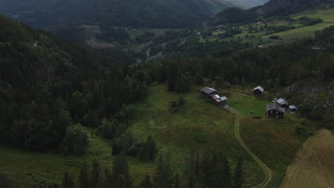 Drone-flies-backward-and-capture-few-small-cottage-at-the-valley-of-Telemark,-Norway-which-is-surrounded-by-the-trees