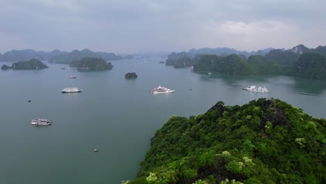 aerial-flying-over-limestone-mountains-revealing-cruise-ships-in-Ha-Long-Bay-Vietnam-on-cloudy-day-surrounding-tropical-water