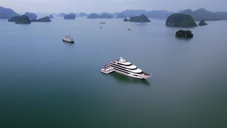 aerial-of-large-white-mega-yacht-anchored-in-Ha-Long-Bay-Vietnam-surrounded-by-large-limestone-cliffs