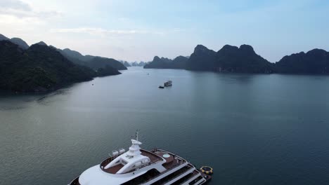aerial-drone-flying-over-white-luxury-yacht-anchored-in-Ha-Long-Bay-Vietnam-in-tropical-blue-water-at-sunset