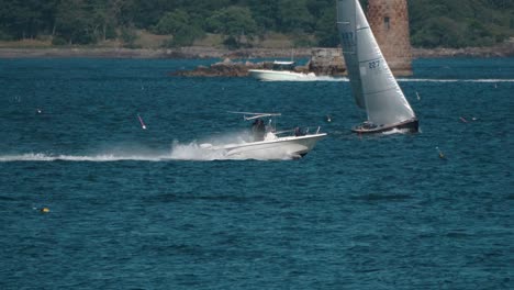 A-speedboat-quickly-moves-through-ocean-water-in-front-of-rocky-shore-and-other-boats-as-camera-tracks
