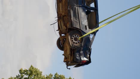 Destroyed-car-is-lifted-in-air-with-crane-for-recycling,-vertical-video