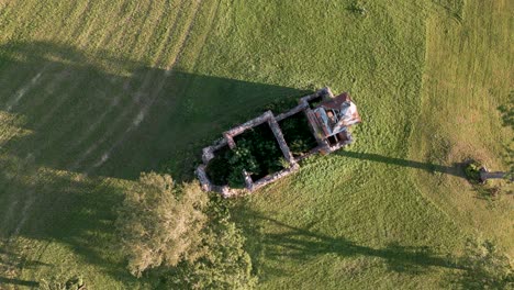 bird-view-top-shot-of-orthodox-or-catholic-lost-place-church-ruin-without-roof-and-trees-inside-on-a-green-mowed-meadow-in-Estonia,-Europe---aerial-drone-flight-flyover-2022