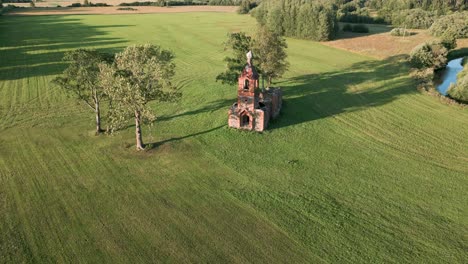 Ascending-aerial-drone-flight-over-an-old-lost-place-church-in-Estonia,-Europe---sand-stone-orthodox-or-catholic-church-ruin-in-summer-2022-next-to-a-country-road-with-moving-cars---bird-view