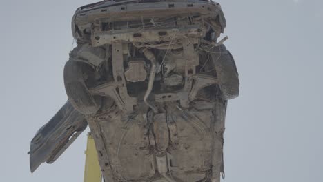 Car-wreck-lifted-high-above-for-recycle,-bottom-view-against-sky