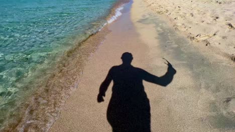 Silhouette-Schatten-Eines-Mannes,-Der-Eine-Sonnenbrille-Abnimmt-Und-Am-Sandstrand-Entlang-Der-Türkisfarbenen-Meerwasserküste-Spazieren-Geht