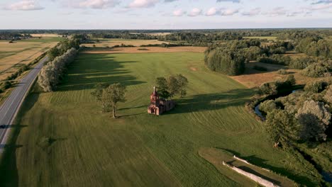 Aerial-drone-flyover-baltic-country-side-of-Estonia,-Europe-with-a-orthodox-or-catholic-lost-place-church-ruin-without-roof-on-a-green-meadow-next-to-country-road-with-cars-on-a-hot-summer-day-2022