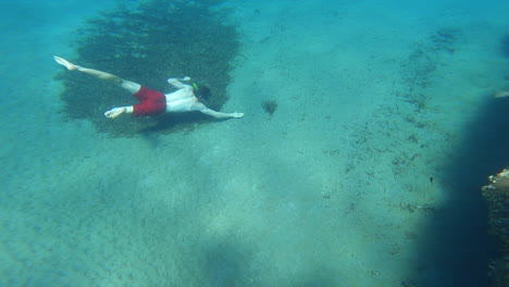 Un-Joven-Buceador-Está-Nadando-Bajo-El-Agua-En-El-Mar-Mediterráneo,-Tocando-Arena-En-El-Fondo