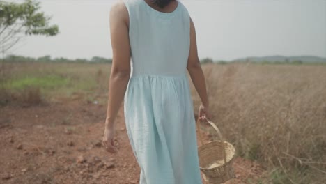 Close-up-shot-of-a-woman-in-a-blue-dress-walking-in-a-field-with-a-basket-in-her-hand