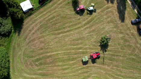 Several-tractors-collecting-straw-bales-on-green-meadow-during-sunny-day