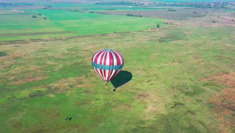 Flying-around-colorful-air-balloon-which-is-about-to-take-off-from-a-green-field