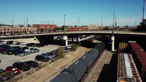 Drone-video-shows-a-freight-train-transporting-goods-on-land-via-tracks,-as-well-as-many-cars-parked-along-the-side-and-a-flyover