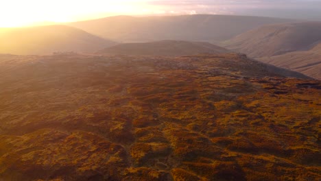 Cinematic-drone-flight-over-moor-landscape-on-top-of-Kinder-Scout-Mountains-at-Peak-district-in-England---Sun-rays-in-Background-during-sunset