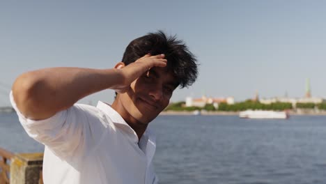 Smart-young-Asian-businessman,-student,-smiling-in-camera-at-river-in-city-Riga