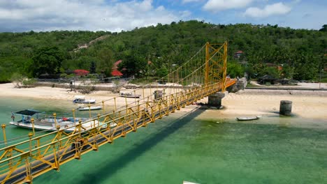 aerial-of-tourists-driving-scooters-across-a-yellow-suspension-bridge-from-Nusa-Ceningan-to-Lembongan-island-on-sunny-day-in-Bali-Indonesia