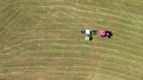 Luftaufnahme-Aus-Der-Vogelperspektive-Des-Traktors,-Der-Einen-Eingewickelten-Heuballen-über-Die-Grüne-Wiese-In-Chmielno-Zieht