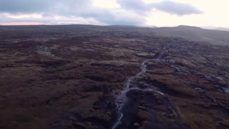 Aerial-flyover-river-flowing-along-Kinder-Scout-moorland-plateau-in-England-during-cloudy-day
