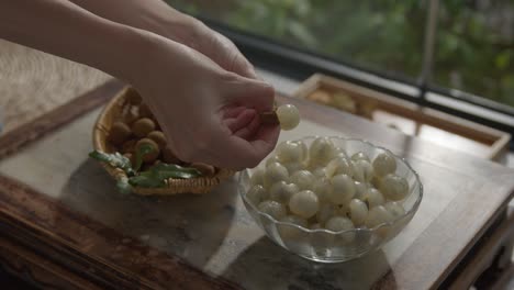 Person-peeling-longan-fruit-and-putting-it-in-bowl-on-table