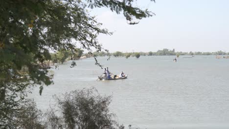 View-Through-Tree-Branches-Of-Boat-Carrying-People-On-Flooded-Landscape-In-Maher,-Sindh