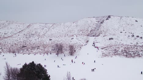 Drohnenaufnahme-Von-Menschen,-Die-Im-Winter-Auf-Einem-Schneebedeckten-Hügel-Spielen