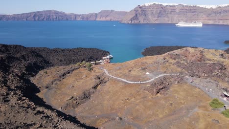 Flying-down-to-little-harbor-of-volcano-island-in-Santorini,-Greece-in-slow-motion