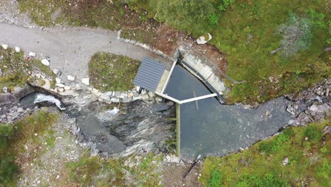Birdseye-view-of-a-small-water-intake-to-river-base-hydroelectric-powerplant-at-Markaani-plant-in-Vaksdal-Norway---Top-down-view-from-intake-to-water-pipe-high-up-in-the-mountains