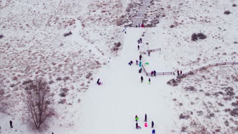 Antenne-Eines-Schneebedeckten-Hügels-Mit-Tonnen-Von-Kindern,-Die-Im-Frischen-Pulver-Spielen