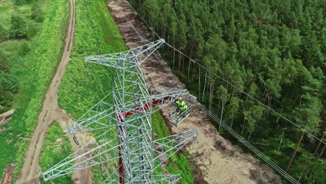 Aerial-top-down-of-industrial-worker-in-lift-crane-repairing-transmission-tower-in-woodland