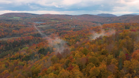 Aerial-fly-over-shot-watching-the-fog-rise-from-the-colorful-hills-in-Vermont,-New-England-in-the-Fall
