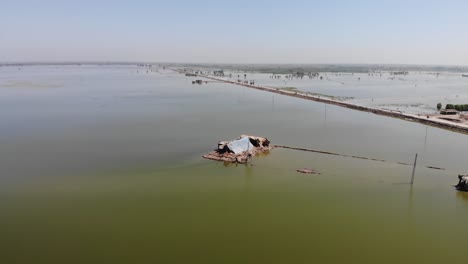 In-Pakistan,-a-drone-captures-an-aerial-shot-of-a-desolate,-damaged-house-and-the-field-around-it-that-has-been-submerged-by-water