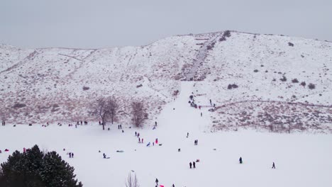 Drone-shot-of-children-playing-on-a-snowy-hill-in-Boise,-Idaho