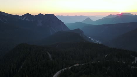 Die-Drohne-Nimmt-Eine-Luftaufnahme-Des-Mount-Rainier-National-Park-Und-Im-Hintergrund-Auf,-Während-Die-Sonne-Am-Horizont-Aufgeht