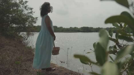 Shot-of-a-women-close-to-the-river-with-a-blue-dress-and-a-basket-in-the-hands-looking-towards-the-camera