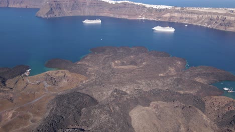 High-altitude-aerial-overview,-tilting-down-over-volcano-crater-at-Santorini-island,-Greece-in-slow-motion