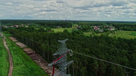 Aerial-flight-towards-worker-hanging-on-transmission-tower-and-working-in-forest-landscape