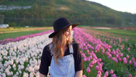 Woman-standing-in-field-of-tulips-with-large-hat-at-sunrise-in-nice-light-in-Abbotsford,-British-Columbia,-Canada