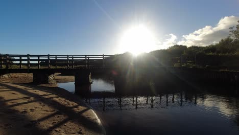 Time-lapse-sunset-clouds-mirrored-under-wooden-bridge-flowing-beach-creek