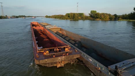 Cargo-ship-with-side-attached-barge-passing-on-river-in-golden-hour
