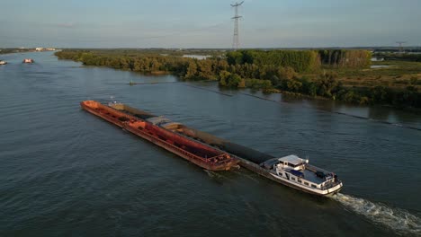 Aerial-slide-and-pan-footage-of-long-cargo-ship-transporting-bulk-material-in-barges-on-river-in-flat-landscape