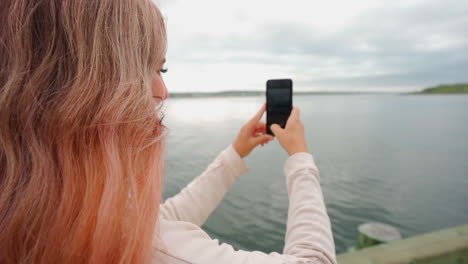 Woman-with-pink-hair-on-the-coast-of-eastern-Canada-taking-a-photo-on-heriphone-during-midday