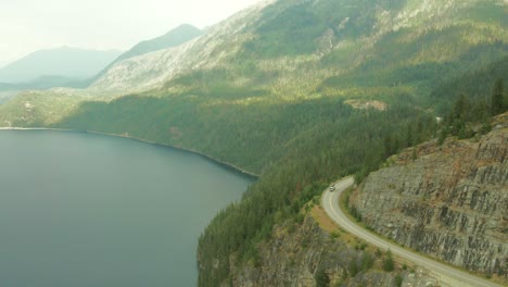 Aerial-dolly-shot-showing-cars-driving-past-Slocan-Lake,-Canada