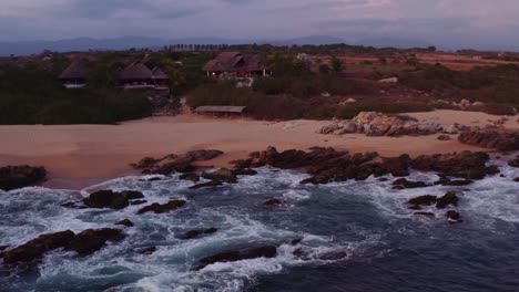 Drone-shot-waves-crash-into-beach-in-front-of-luxurious-villas-in-Mexico